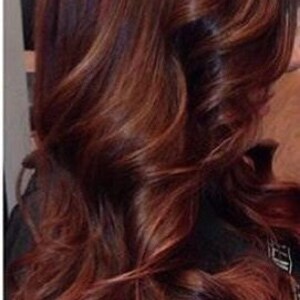 May include: Long, wavy hair with a rich auburn color. The hair is styled in loose waves and has a subtle ombre effect, with darker roots and lighter ends.