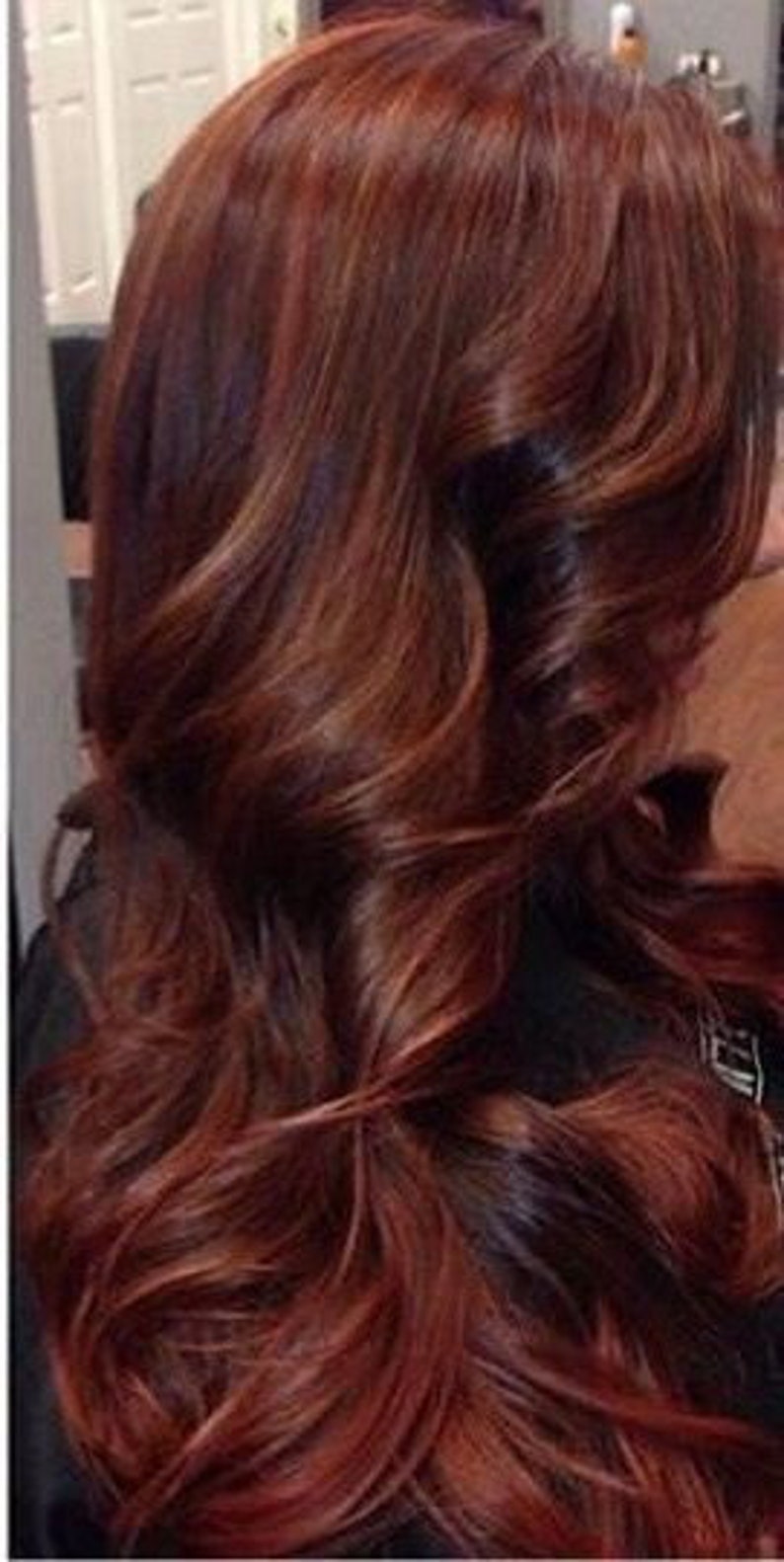 May include: Long, wavy hair with a rich auburn color. The hair is styled in loose waves and has a subtle ombre effect, with darker roots and lighter ends.