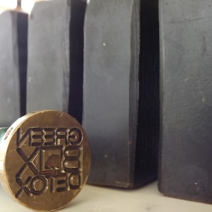 May include: Four black rectangular bars of soap with the words "Green Detox" embossed on a brass stamp.