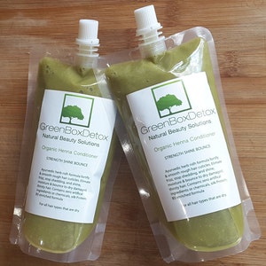 May include: Two green pouches of organic henna conditioner from GreenBoxDetox Natural Beauty Solutions. The pouches are labeled "Strength Shine Bounce" and contain an Ayurvedic herb-rich formula to fortify and smooth hair.