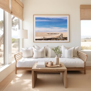 Pu&ograve; includere: Un divano bianco con una struttura in legno e cuscini color marrone chiaro si trova in un soggiorno con una grande finestra. Una fotografia incorniciata di un paesaggio con un cielo blu e nuvole bianche &egrave; appesa al muro sopra il divano. Un tavolino da caff&egrave; in legno con un vassoio e una tazza si trova davanti al divano.