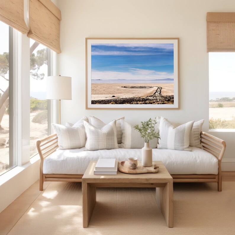 Pu&ograve; includere: Un divano bianco con una struttura in legno e cuscini color marrone chiaro si trova in un soggiorno con una grande finestra. Una fotografia incorniciata di un paesaggio con un cielo blu e nuvole bianche &egrave; appesa al muro sopra il divano. Un tavolino da caff&egrave; in legno con un vassoio e una tazza si trova davanti al divano.