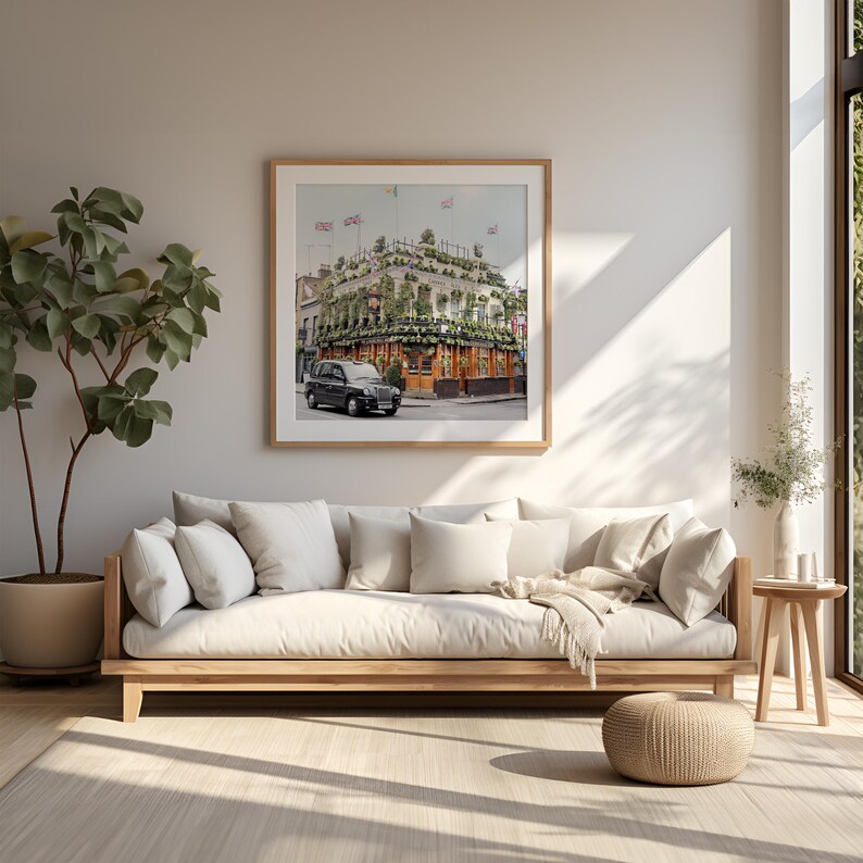 May include: A white linen sofa with a wooden frame and a throw blanket. The sofa is in a living room with a framed print of a building with a black taxi in front of it.