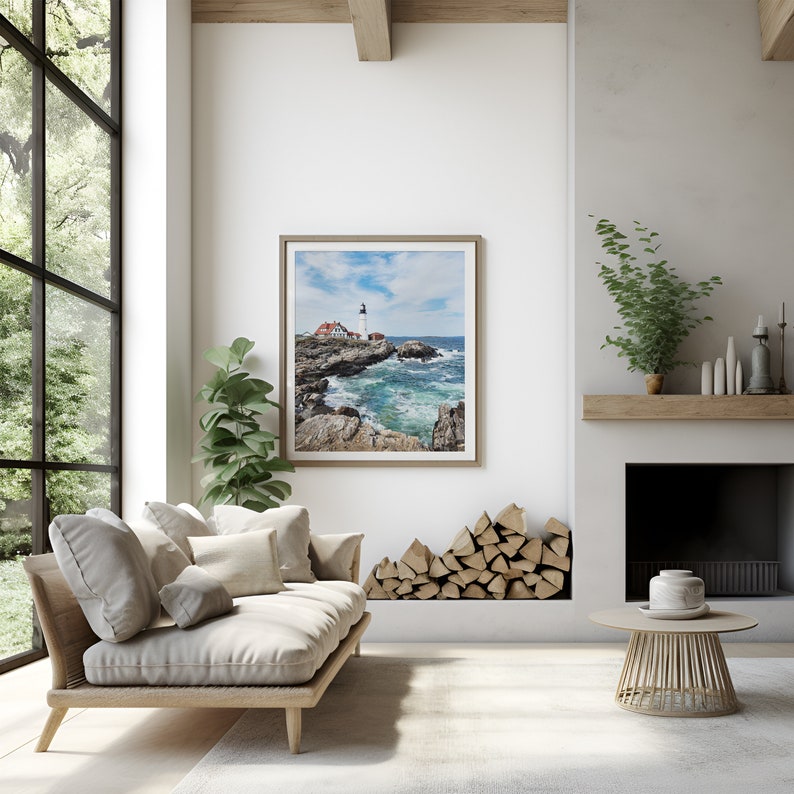 May include: A light wood couch with beige cushions sits in a living room with a large window, a fireplace, and a framed photograph of a lighthouse on a rocky coast.