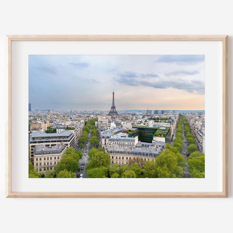 May include: A framed print of Paris, France, showing the Eiffel Tower. The image captures a wide view of the city, with tree-lined streets and buildings. The sky displays a blend of blue and pastel hues.