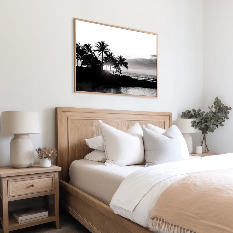 Pode incluir: Fotografia em preto e branco de palmeiras silhuetas contra um c&eacute;u de p&ocirc;r do sol. A foto est&aacute; emoldurada e pendurada em uma parede branca acima de uma cama de madeira com roupa de cama branca.