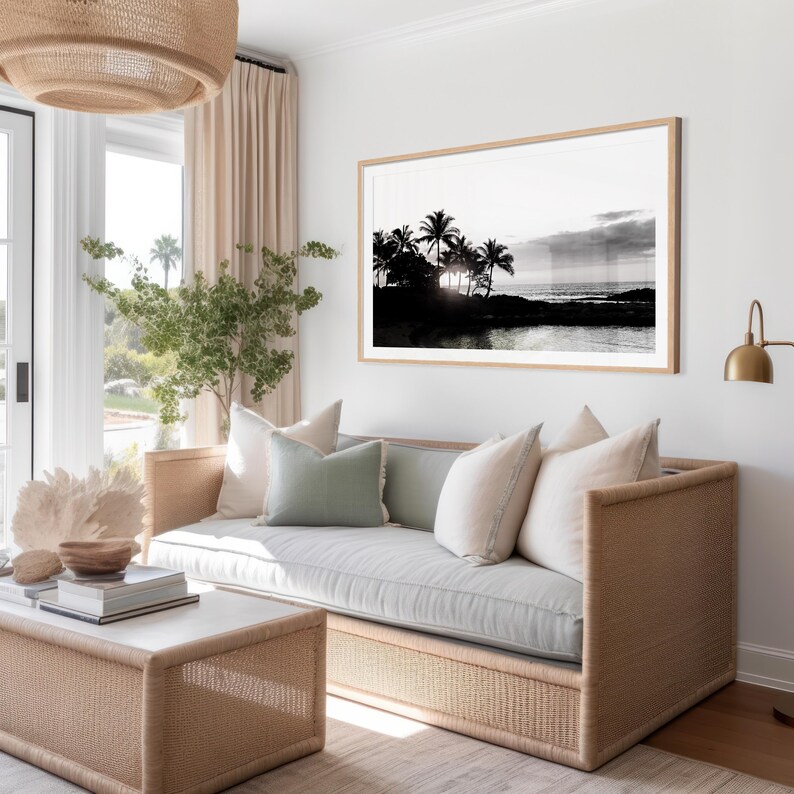 Pode incluir: Um sof&aacute; cinza claro com uma estrutura de vime tecida e almofadas de cor verde claro e branco. O sof&aacute; est&aacute; em uma sala de estar com uma grande fotografia em preto e branco de uma cena de praia tropical pendurada na parede.