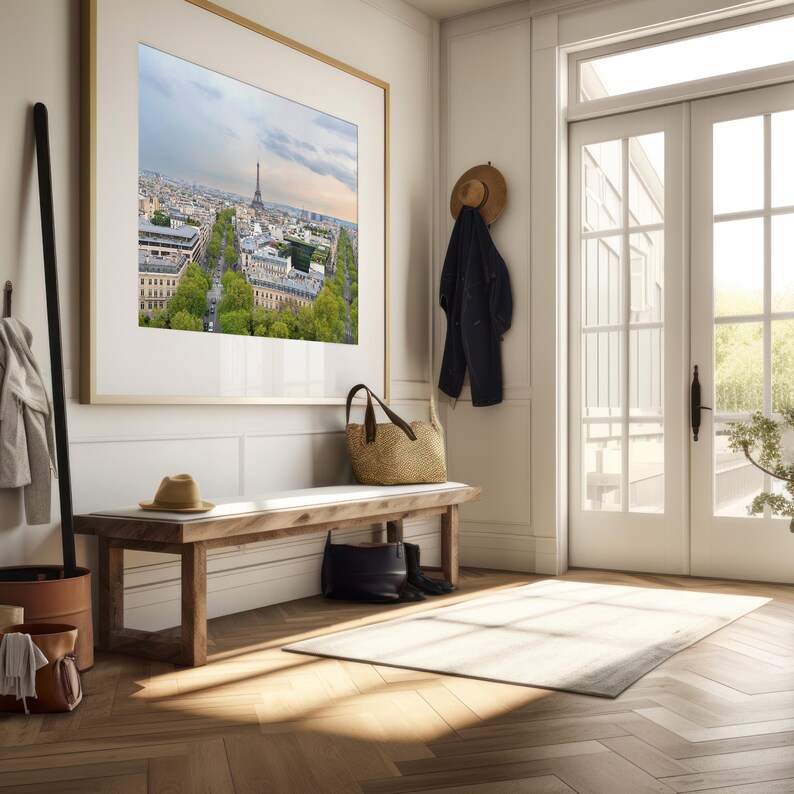 May include: A framed print of the Eiffel Tower and Paris cityscape hangs above a wooden bench. A straw bag, hat, and black boots sit on the bench. A coat and hat hang on the wall, and a rug lies on the herringbone floor.