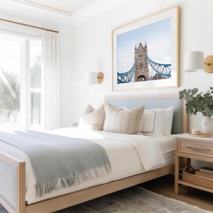 May include: A light blue bed with a white duvet and a light blue throw blanket. The bed has a light wood frame and a light blue headboard. There is a framed print of the Tower Bridge above the bed.