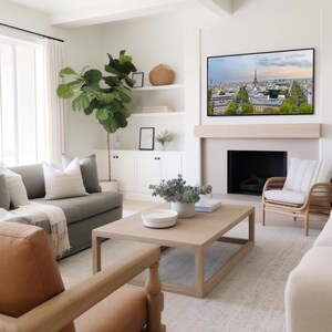 May include: A contemporary living room with a large television above a fireplace. The room includes a grey sofa, a wooden coffee table, and a woven armchair. A large potted plant and decorative items create a comfortable and stylish atmosphere.