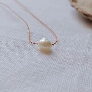 May include: A single white, irregularly shaped freshwater pearl centered on a thin, metallic copper-colored cord necklace. The pearl features a smooth, lustrous surface, while the delicate cord provides a simple, understated contrast to the pearl.