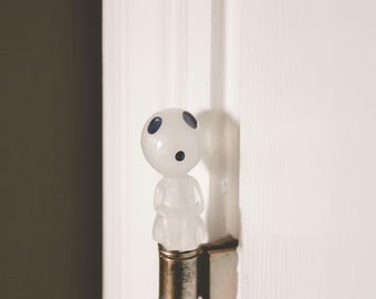 May include: A white ceramic figurine with blue eyes, resembling a character from the movie "My Neighbor Totoro", is attached to a silver door hinge.