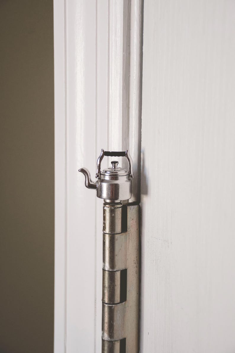 May include: A silver teapot with a black handle is attached to a silver door hinge.