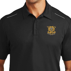 May include: Black polo shirt with a gold and black emblem on the left chest. The shirt has a three-button placket and short sleeves. The collar and shoulders have a gray accent stripe. The person is wearing a black belt and black pants.