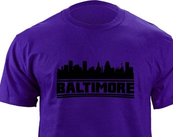 May include: Purple t-shirt with a black silhouette of the Baltimore skyline and the word "BALTIMORE" printed in black.