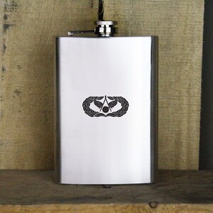 May include: A silver stainless steel flask with a black engraved Air Force Airman's Badge.