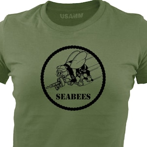 May include: A green t-shirt with a black and white graphic of a cartoon bee holding a gun. The graphic is surrounded by a rope circle and the text "SEABEES" is printed below the bee.