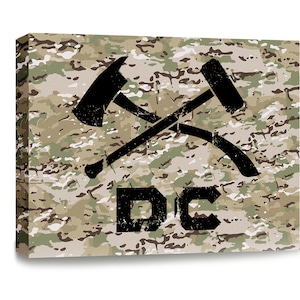 May include: A camouflage background with a black axe and hammer crossed over each other. The letters "DC" are below the crossed tools.