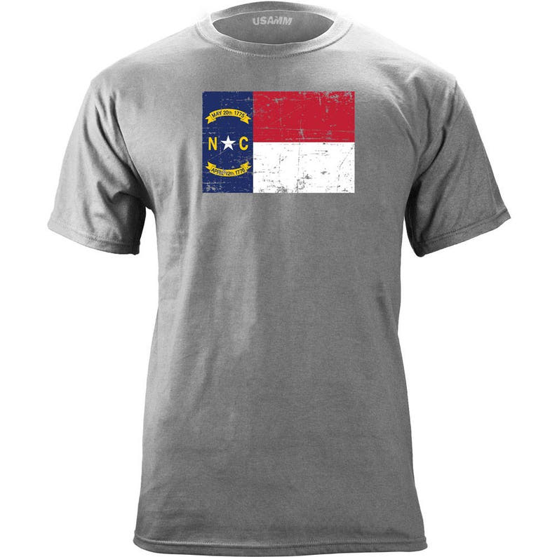 May include: A grey t-shirt with a distressed vintage North Carolina state flag design. The flag features a blue star in a yellow circle with the letters "N.C." and the words "May 20, 1775" and "April 12, 1776".