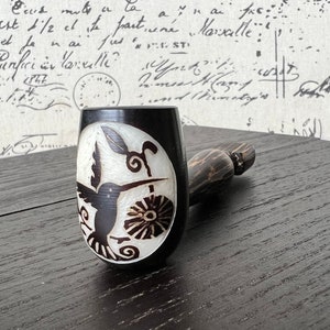 May include: A wooden smoking pipe with a black and white hummingbird design on the bowl. The pipe is made of dark wood and has a natural finish.