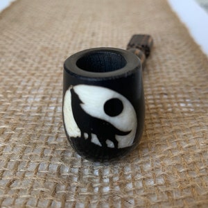 May include: A black wooden pipe with a white wolf howling at the moon design.