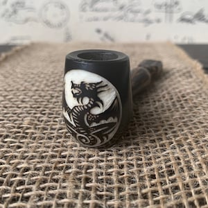 May include: A black wooden smoking pipe with a white inlay of a dragon design.