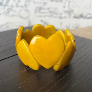 May include: A yellow heart-shaped bracelet made of plastic. The bracelet is made up of multiple heart-shaped pieces that are connected together.