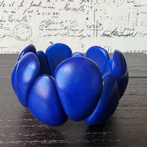 May include: A vibrant blue statement bracelet. The bracelet features large, rounded, organic-shaped links, creating a bold and eye-catching design. The glossy finish enhances the rich color. This piece is a striking accessory.