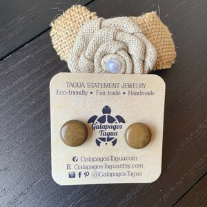 May include: A pair of brown tagua nut earrings with a turtle logo and the text "Galapagos Tagua" on the card. The card also includes the text "Eco-friendly, Fair trade, Handmade" and the website address "Galapagos Tagua.com".