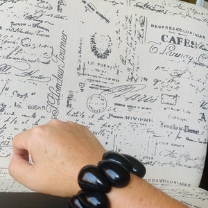 Pode incluir: Um bracelete de contas pretas com contas grandes de forma oval. O bracelete &eacute; usado no pulso.
