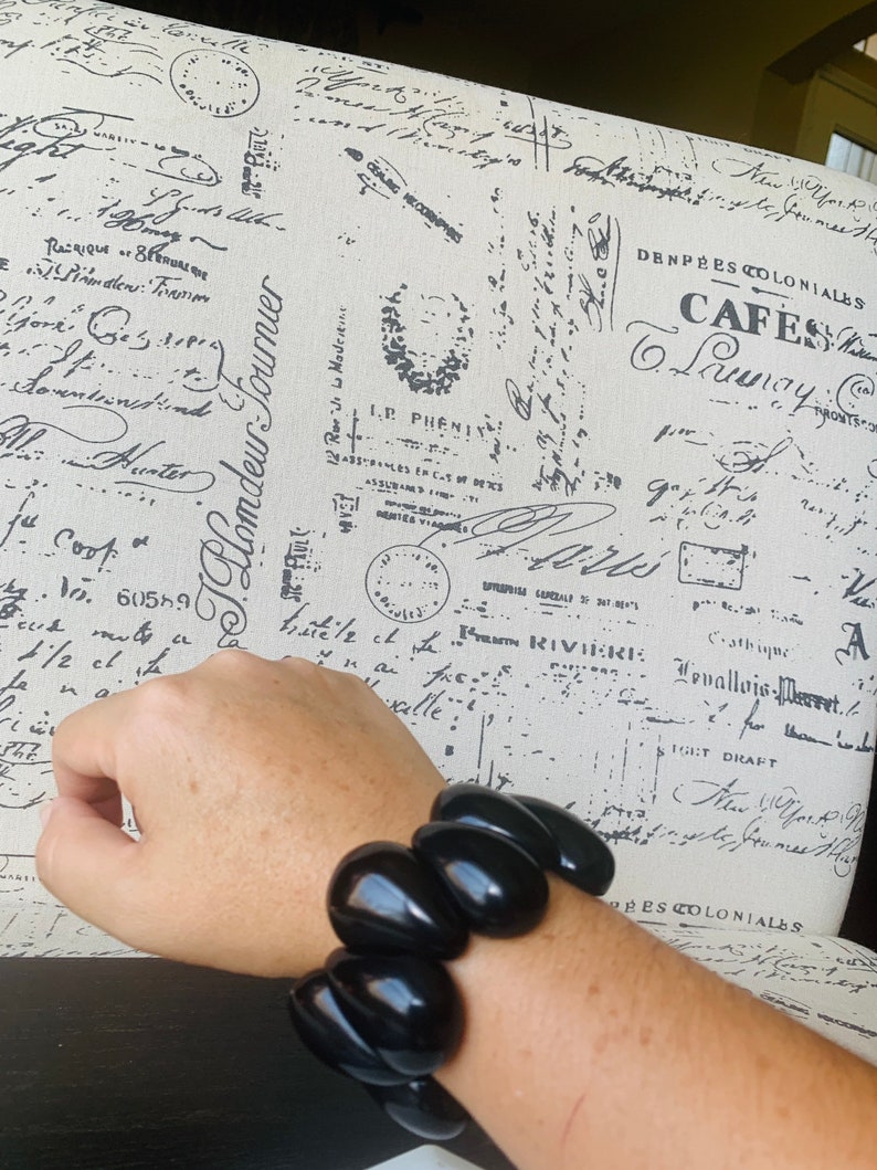 Pode incluir: Um bracelete de contas pretas com contas grandes de forma oval. O bracelete &eacute; usado no pulso.