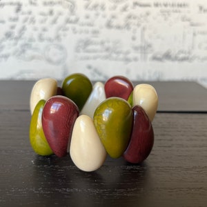 Pode incluir: Um bracelete feito de contas lisas, arredondadas, em forma de l&aacute;grima em tons de verde, marrom e branco.