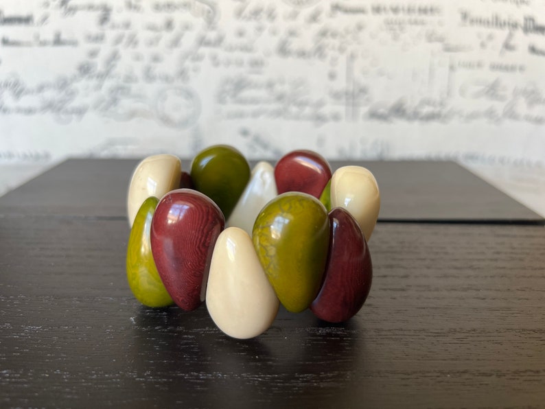 Pode incluir: Um bracelete feito de contas lisas, arredondadas, em forma de l&aacute;grima em tons de verde, marrom e branco.