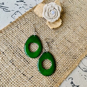 May include: A pair of green avocado-shaped earrings with a silver hook and a circle cut out of the center.