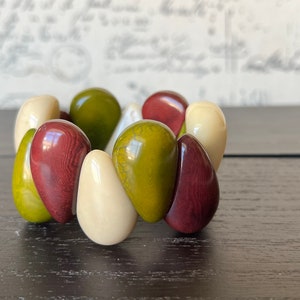 Pode incluir: Um bracelete feito de contas lisas, arredondadas, em forma de l&aacute;grima em tons de verde, creme e bord&ocirc;.