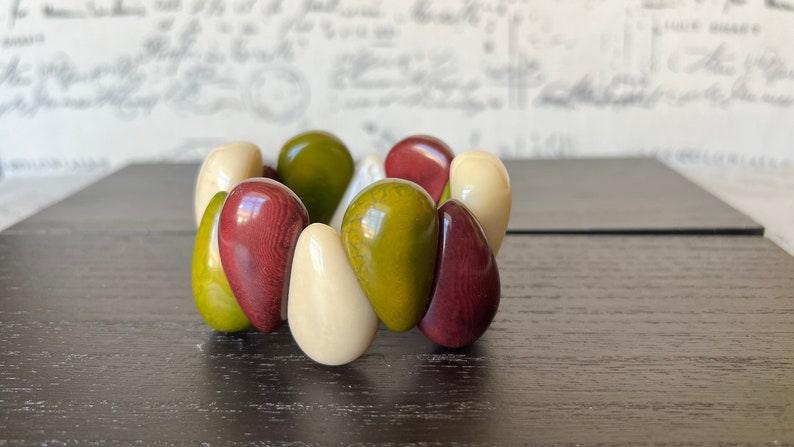 Pode incluir: Um bracelete feito de contas lisas, arredondadas, em forma de l&aacute;grima em tons de verde, creme e bord&ocirc;.
