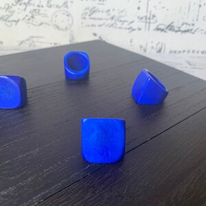 May include: Four blue square-shaped rings on a dark wood surface. The rings are made of a smooth, polished material.