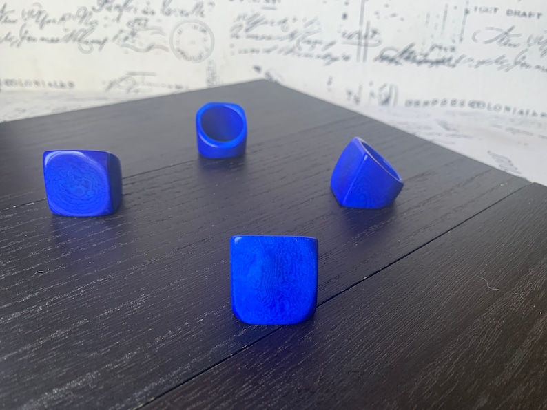 May include: Four blue square-shaped rings on a dark wood surface. The rings are made of a smooth, polished material.