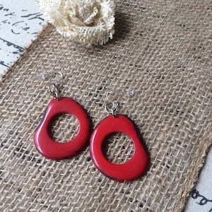 May include: A pair of red, irregular shaped earrings with a silver hook. The earrings have a black outline and a ring in the center.