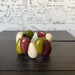 Pode incluir: Um bracelete feito de contas verdes, marrons e brancas. As contas est&atilde;o dispostas em um padr&atilde;o circular.