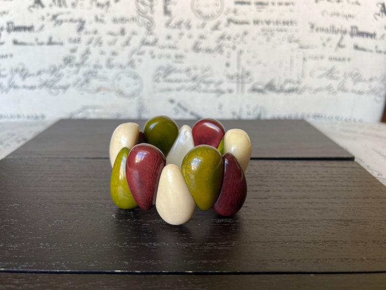 Pode incluir: Um bracelete feito de contas verdes, marrons e brancas. As contas est&atilde;o dispostas em um padr&atilde;o circular.