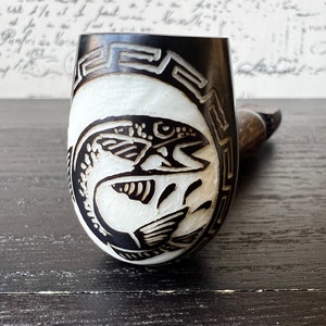 May include: A black and white wooden pipe with a carved fish design. The pipe bowl is decorated with a geometric pattern.