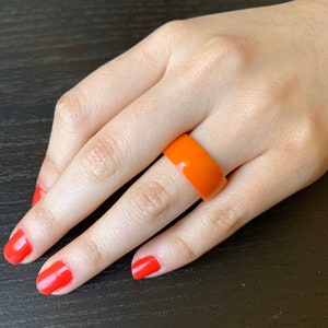 May include: A wide orange plastic ring worn on a finger.