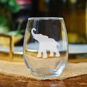 May include: A clear glass wine glass with an etched design of a white elephant. The elephant is facing to the right and has its trunk raised.