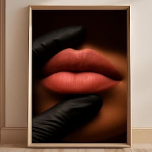 Op de afbeelding: Een ingelijste print met een close-up van rode lippen. Een zwart gehandschoende hand bedekt de lippen gedeeltelijk. De afbeelding heeft een donkere achtergrond, wat een opvallend contrast creëert. De lijst is licht van kleur.