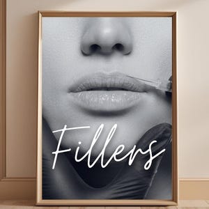 May include: Black and white framed print featuring a close-up of a person's lips receiving an injection. The word "Fillers" is written in a cursive font across the image. The image is displayed in a room with wooden floors and shelves.