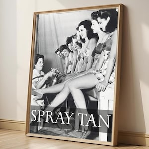 May include: Framed black and white print featuring a vintage image of women getting spray tans. The image shows a group of women in swimwear, with one person applying the tan. The text "SPRAY TAN" is displayed.