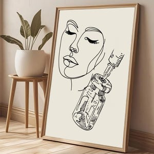 May include: A framed art print with a minimalist line drawing of a face and a vial with a syringe. The artwork is in black and white, with the face in profile and the vial detailed with lines. The frame is a light wood colour.