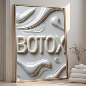 Könnte beinhalten: Ein gerahmtes Kunstwerk mit dem Wort "BOTOX" in erhabenen weißen Buchstaben. Der Hintergrund zeigt fließende, abstrakte weiße Formen. Der Rahmen ist goldfarben, und das Kunstwerk lehnt an einer Wand. Ein Stapel weißer Handtücher und eine Vase mit Trockenblumen befinden sich in der Nähe.