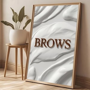 May include: A framed print with the word "Brows" in a 3D brown font against a white, textured backdrop. The artwork is in a light brown wooden frame, leaning against a wall. A small potted plant sits on a wooden side table.